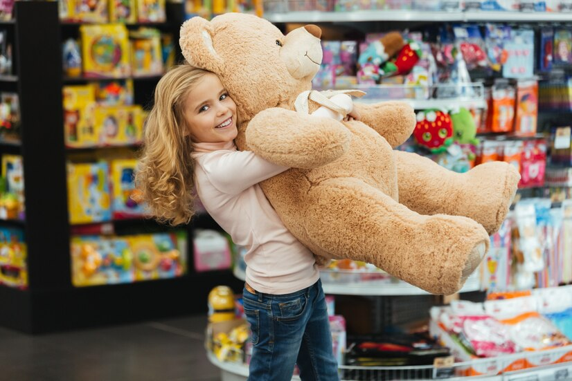 Uma garotinha sorridente segurando um grande urso de pelúcia em uma loja de brinquedos