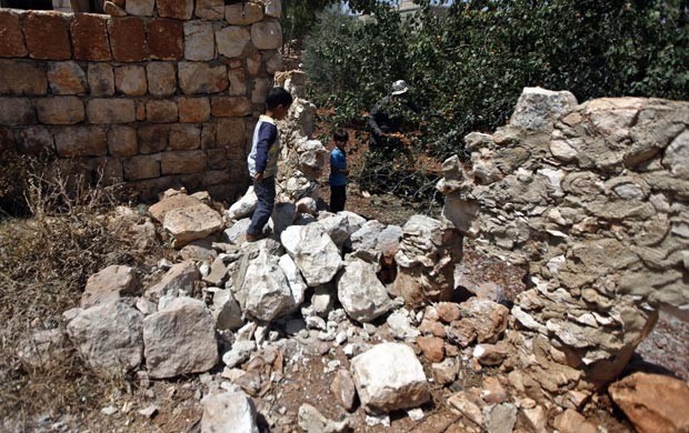 Crianças caminham pelos destroços de muro que teria sido derrubado por ataque de helicóptero nesta quinta-feira (14) na cidade síria de Idlib (Foto: AP)