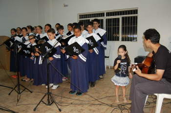 O professor Luciano, a cantora mirim Ana e as crianças e adolescentes do coral.