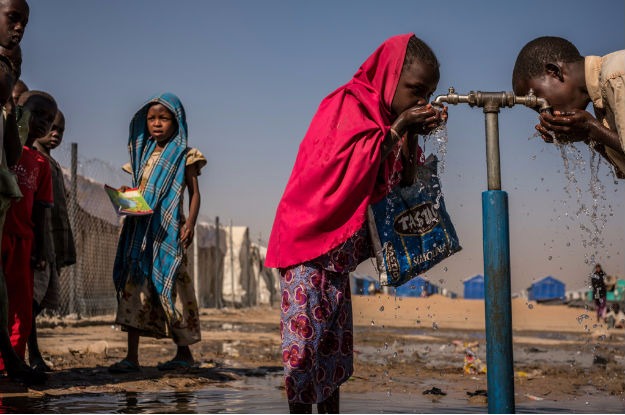 Crianças bebem água em uma torneira durante o recesso em uma escola primária apoiada pelo Unicef dentro do campo para pessoas deslocadas internamente de Bukasi, em Maiduguri, estado de Borno, Nigéria. Foto: Unicef/ Gilbertson