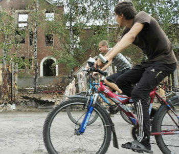 Ciclistas passam por um prédio residencial destruído, na região de Donetsk. Foto: Acnur/I.Zimova