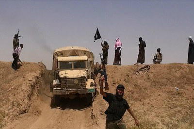 Militantes do Estado Islâmico (IS) acenam a bandeira e segurando suas armas em uma estrada recém-cortada através da fronteira sírio-iraquiana. Foto compartilhada por um jihadista em um perfil no Twitter, em junho 