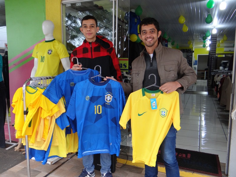 Copa do Mundo é promessa para elevar vendas no comércio amambaiense Acácio e seu colaborador estão animados com a venda de camisetas para a Copa do Mundo / Foto: Moreira Produções