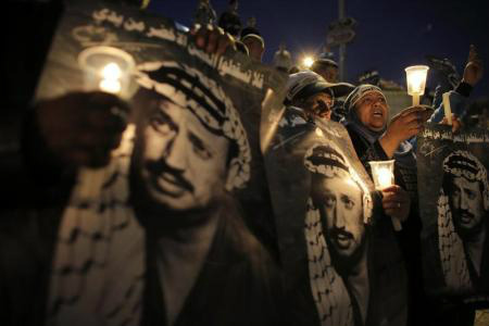 Palestinos seguram velas e cartazes com a imagem do falecido líder palestino Yasser Arafat durante uma manifestação para marcar o 9º aniversário de sua morte, em Jerusalém. 