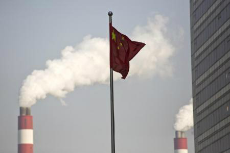 A bandeira da China tremula fora da Zona de Livre Comércio da China, em Xangai, conforme fumaça sai de chaminés na usina termelétrica em Pudong