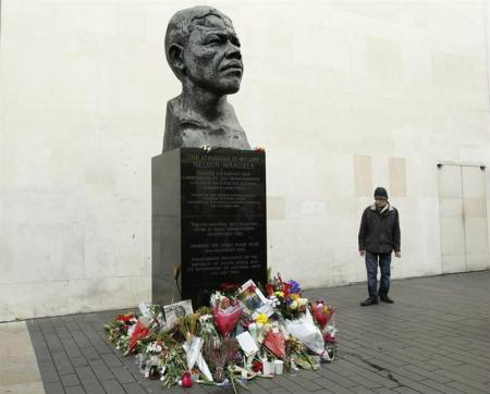Um homem observa flores à esquerda de uma escultura do ex-presidente da África do Sul Nelson Mandela em Londres. 