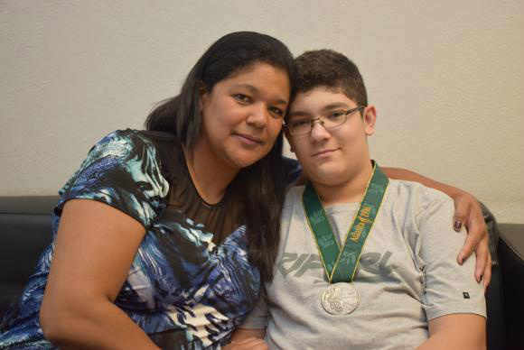 A ex-pivô da seleção brasileira de basquete Claudia Pastor e o filho Maurílio com a medalha de prata conquistada pela mãe na Olimpíada de Atlanta, em 1996 Divulgação/Arquivo pessoal