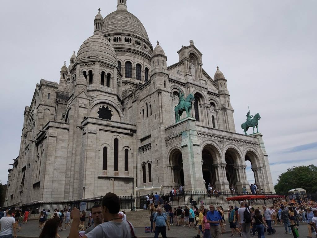 Paris em 10 dias, por Viviane Viaut - parte 1 A Basílica do Sagrado Coração (em francês, basilique du Sacré-Cœur) é um templo da Igreja Católica Romana em Paris, sendo, também, o símbolo do bairro de Monte Martre. A basílica está localizada no topo do monte Martre, o ponto mais alto da cidade. A basílica do Sagrado Coração foi construída com mármore travertino extraído da região de Seine-et-Marne, o que lhe proporciona uma tonalidade branca.Um dos monumentos mais visitados da França, a basílica tem o formato de cruz grega adornada por quatro cúpulas, incluindo a cúpula central de oitenta metros de altura. Na abside, uma torre serve de campanário a um sino de três metros de diâmetro e de mais de 26 toneladas.A arquitetura da basílica é inspirada na arquitetura romana e bizantina e influenciou outros edifícios religiosos do século XX.
