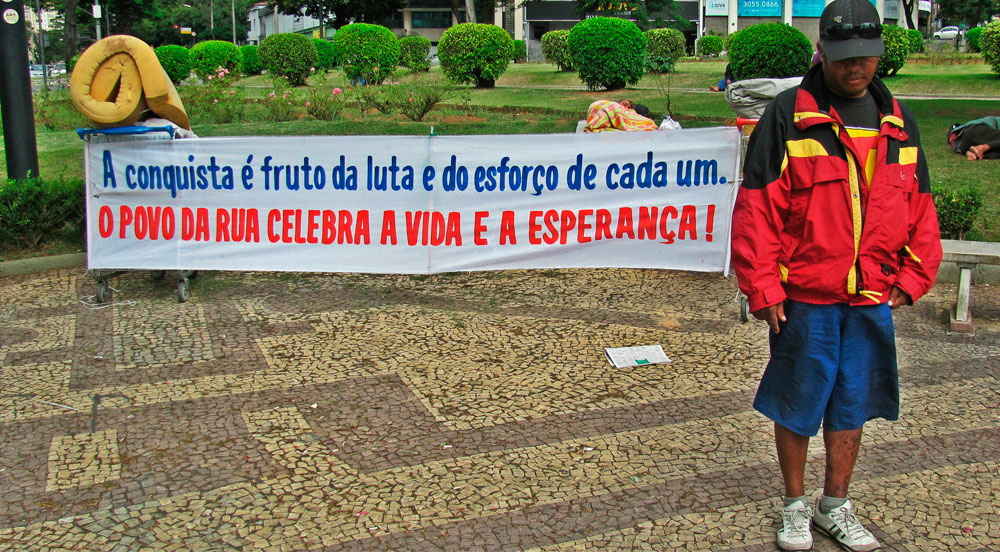 Expulsos das ruas Gil, morador de rua, protesta contra preconceito em praça de Belo Horizonte no dia de abertura da Copa do Mundo. Segundo ele, um policial ameaçou atear fogo aos carrinhos caso não removesse a faixa. (Imagem: Bruno Fonseca: Agência Pública)