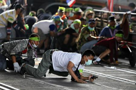 Um manifestante anti-governo armado engatinha durante troca de tiros entre apoiadores do governo e opositores ao governo tailandês, em Bangcoc