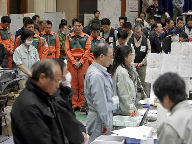 Funcionários da prefeitura de Miyagi, em Sendai, no norte do Japão, param e oram durante um minuto, em homenagem às vítimas dos desastres naturais que completarm uma semana. (Foto: Yomiuri Shimbun / Hirofumi Nagao / AP Photo)