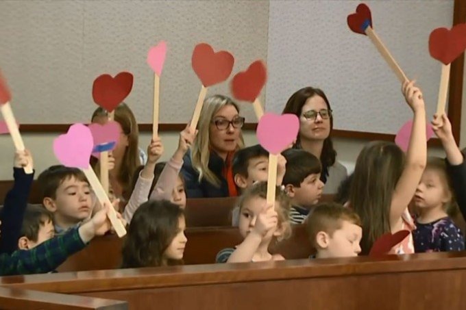 Demonstrando apoio, alunos vão à audiência de adoção de seu colega Os alunos balançavam animados corações colados em palitos (NBC/Reprodução)