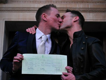 Tim Jarmaine-Groves (à esq.) beija seu marido, Richard Jarmaine-Groves, após obterem seu certificado de casamento em Londres, em 29 de março.
