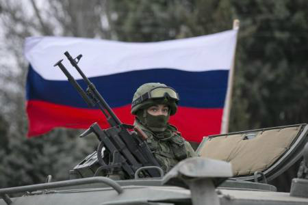 Um ativista pró-Rússia segura uma bandeira russa atrás de um militar armado no topo de um veículo do exército russo, próximo a um posto de controle de fronteira na cidade de Balaclava, na Crimeia. 