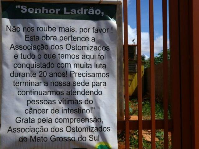 Cansada de furtos, associação apela pedindo compreensão aos ladrões A placa foi colocada no portão da obra na tentativa de sensibilizar e afastar os ladrões. (Foto: André Bittar)