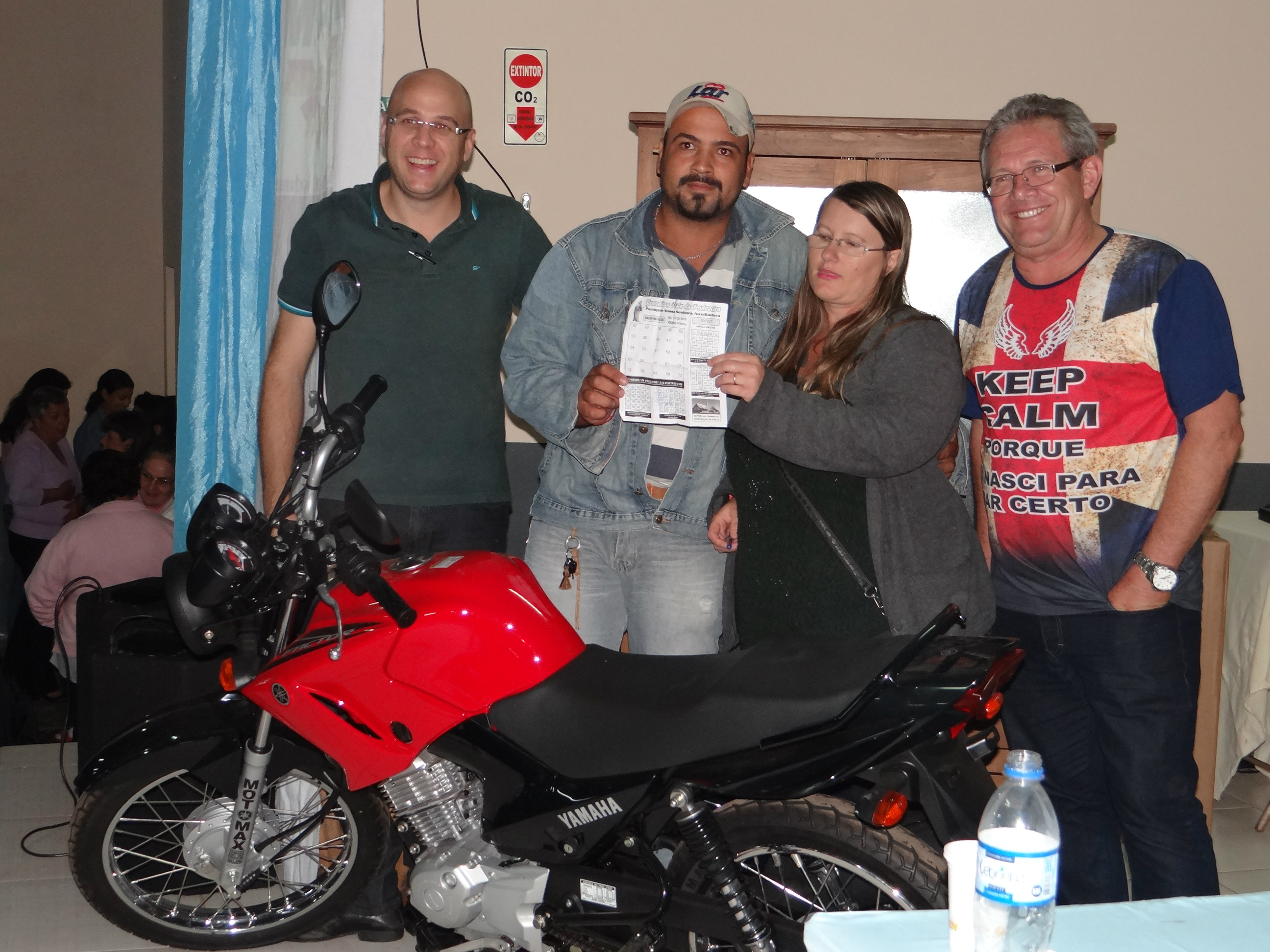 Branco Escobar (D) e Rodrigo Selhorst (E), ambos da comissão organizadora,  com os ganhadores da moto (ao centro).